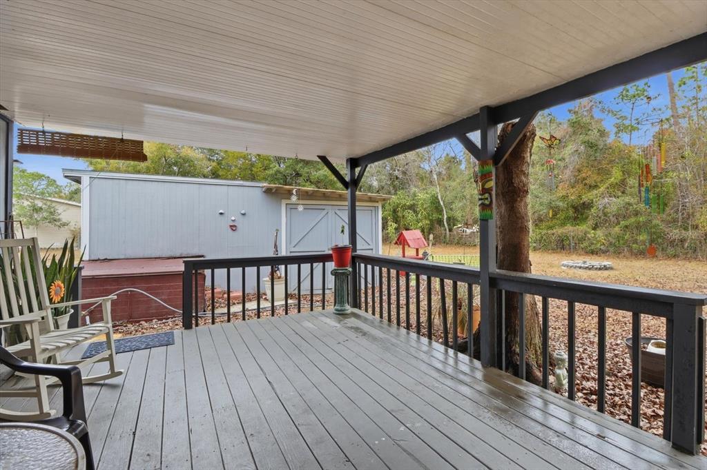 A covered wooden deck features a railing, rocking chairs, and a view of the backyard — 6771 W SASSER STREET, HOMOSASSA, FL