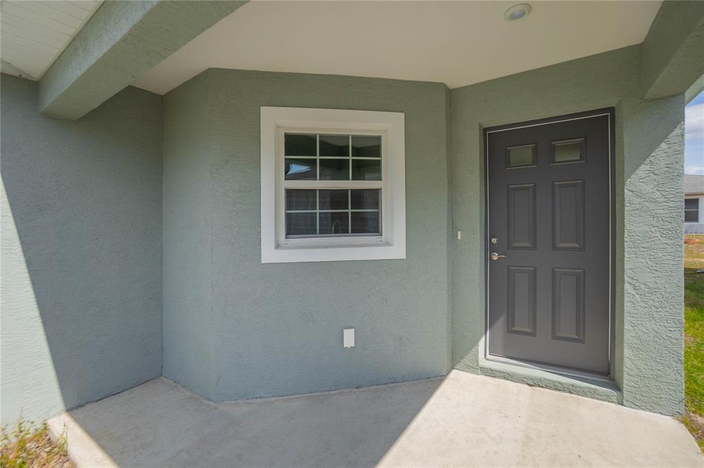 A gray door and a single window are set into the light green stucco exterior — 10494 S DREW BRYANT CIRCLE, FLORAL CITY, FL