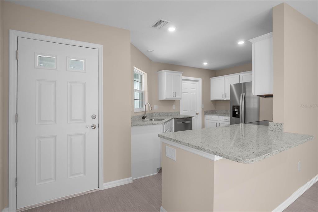 A kitchen with white cabinets, granite countertops, and stainless steel appliances next to an entryway — 10494 S DREW BRYANT CIRCLE, FLORAL CITY, FL