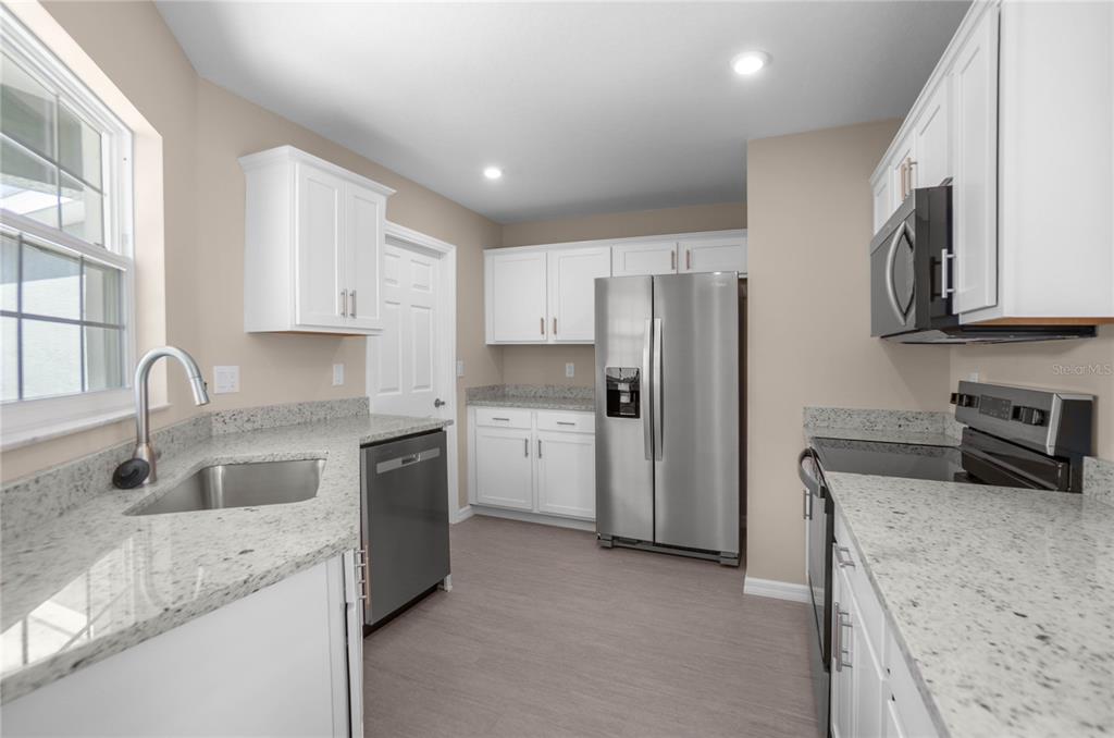 A kitchen with white cabinets, granite countertops, stainless steel appliances, and light wood-look flooring — 10494 S DREW BRYANT CIRCLE, FLORAL CITY, FL