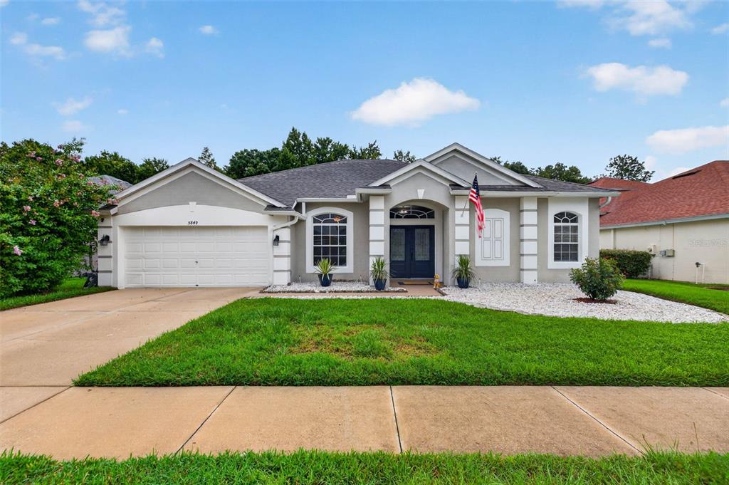 A single-story suburban house with a two-car garage, gray stucco exterior, and a front lawn — 5849 RIVA RIDGE DRIVE, WESLEY CHAPEL, FL