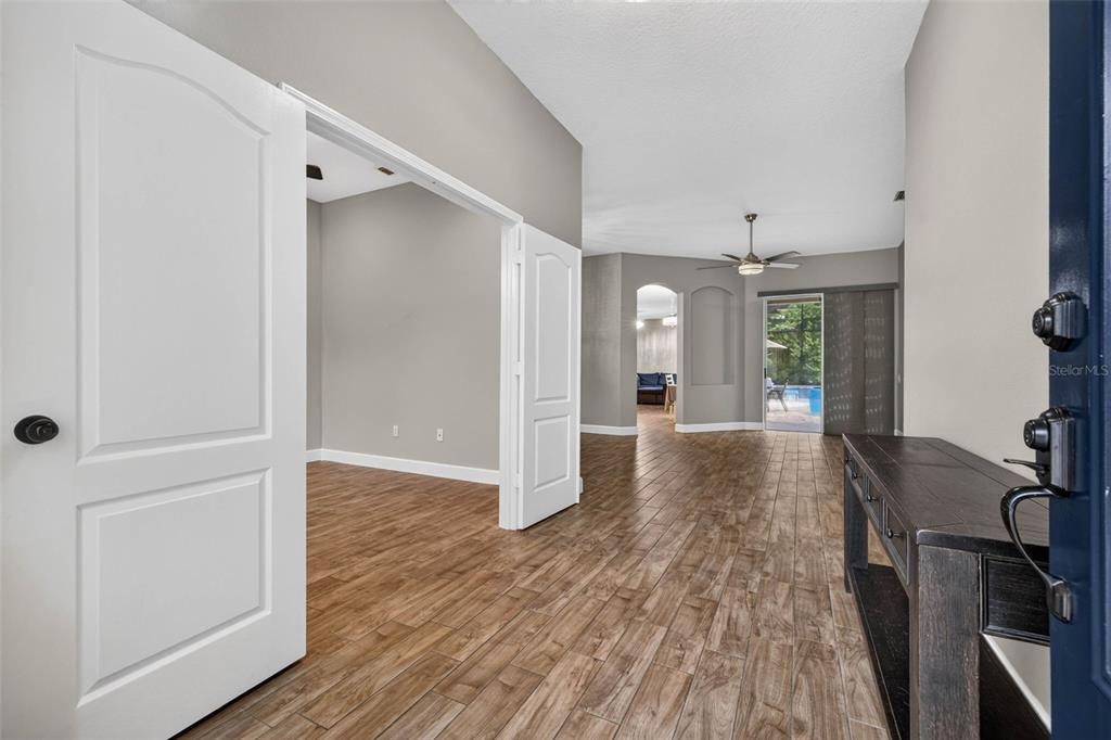 An entryway with wood-look tile flooring leads into an open living area with a pool view — 5849 RIVA RIDGE DRIVE, WESLEY CHAPEL, FL