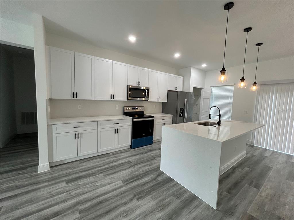 A modern kitchen features white cabinets, stainless steel appliances, a quartz island, and gray flooring — 14445 SW 42ND TERRACE ROAD, OCALA, FL