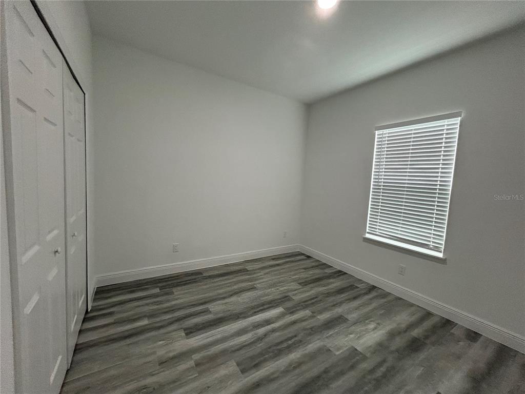 An empty bedroom features white walls, gray wood-look flooring, a window with blinds, and closet doors — 14445 SW 42ND TERRACE ROAD, OCALA, FL