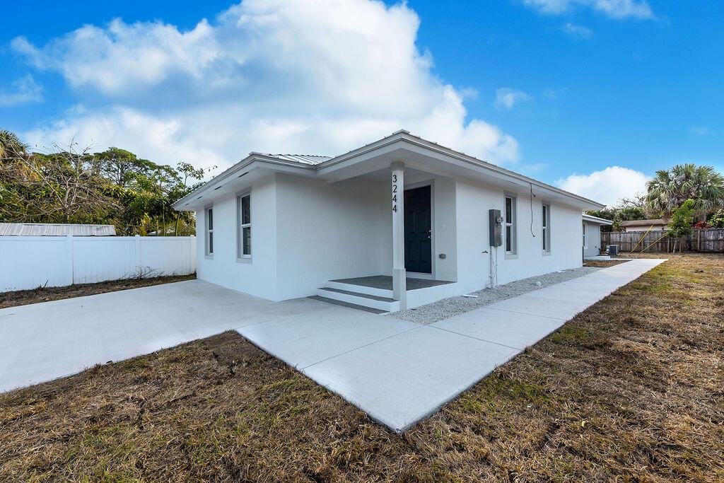 A white, single-story house with a covered entryway and concrete walkway under a blue sky — 3018 SE Iris Street # 1, Stuart FL 34997, STUART, FL
