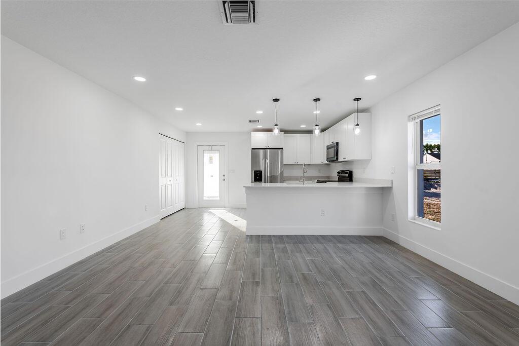 A modern kitchen with white cabinetry and a breakfast bar opens into a living area — 3018 SE Iris Street # 1, Stuart FL 34997, STUART, FL