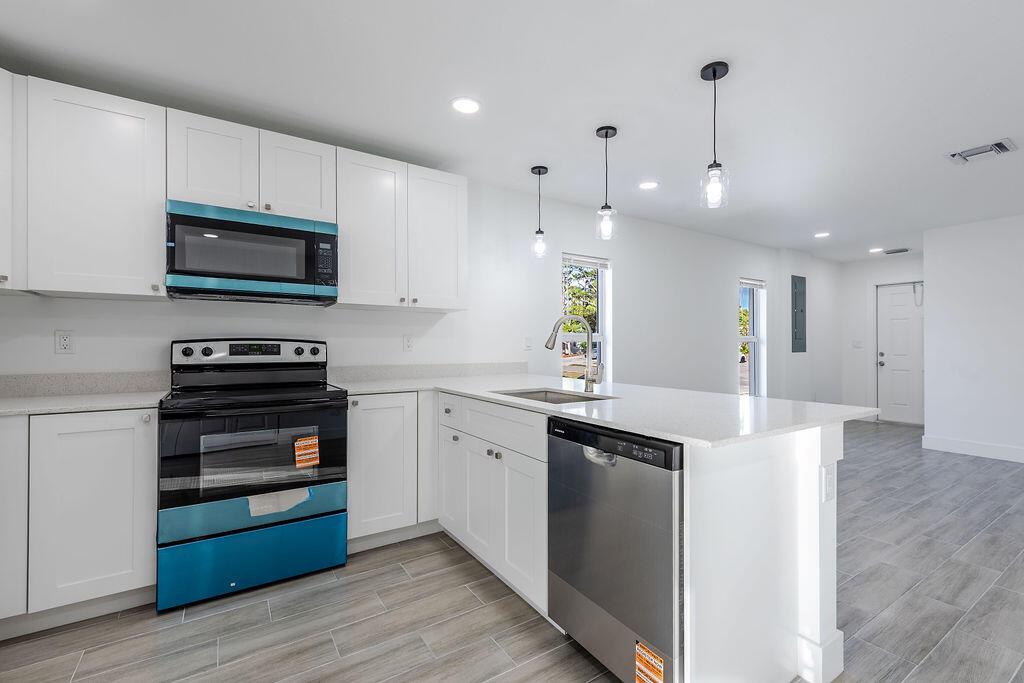 A modern kitchen features white cabinets, stainless steel appliances, and light wood-look tile flooring — 3018 SE Iris Street # 1, Stuart FL 34997, STUART, FL