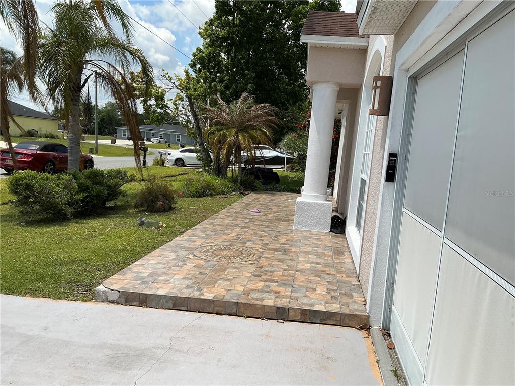A tiled walkway leads to the front entrance of a house with a white pillar — 823 OGNON COURT, KISSIMMEE, FL