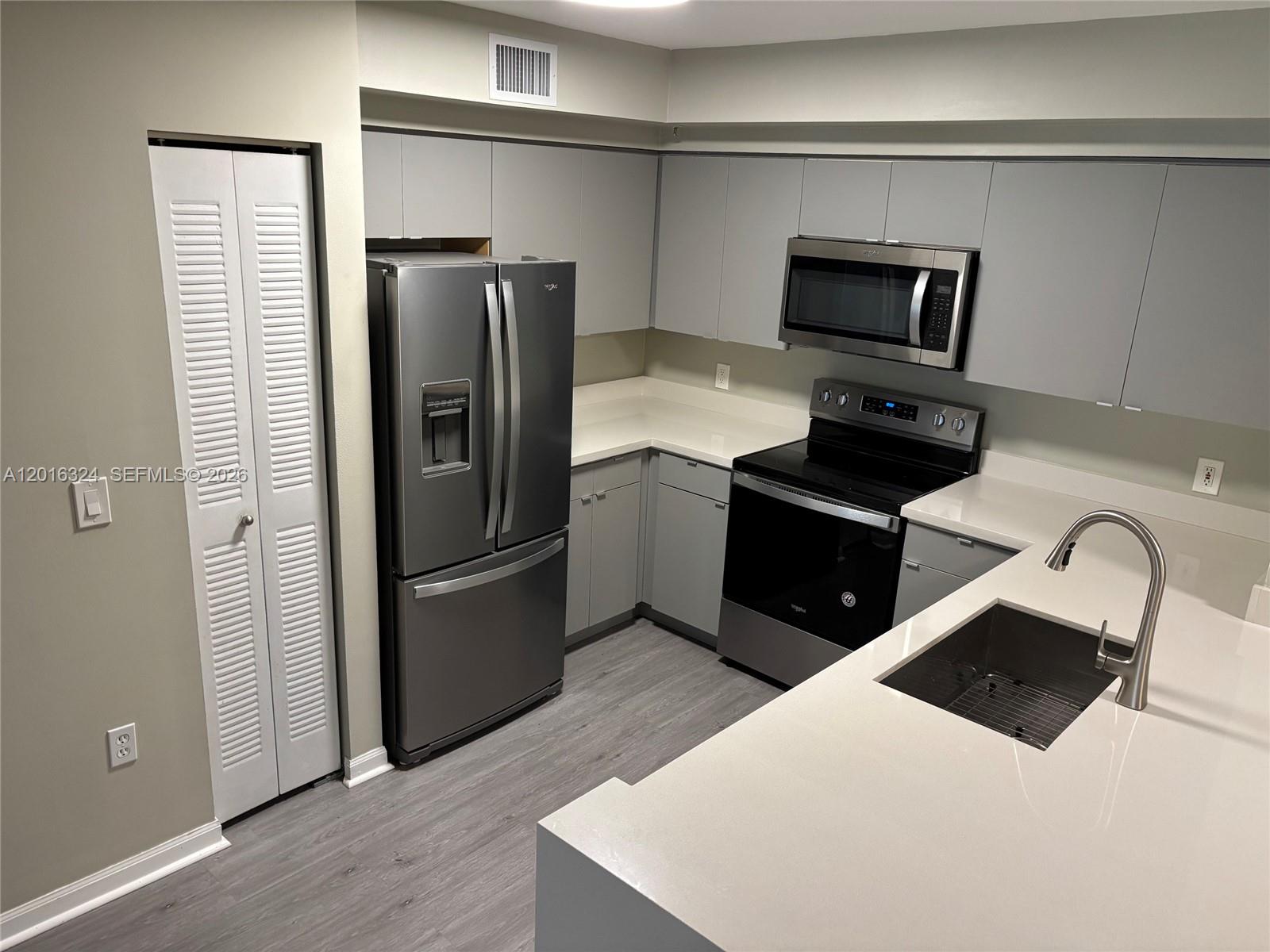 A modern kitchen features gray cabinets, stainless steel appliances, and white countertops — 1900 Van Buren St # 201B, Hollywood FL 33020, HOLLYWOOD, FL