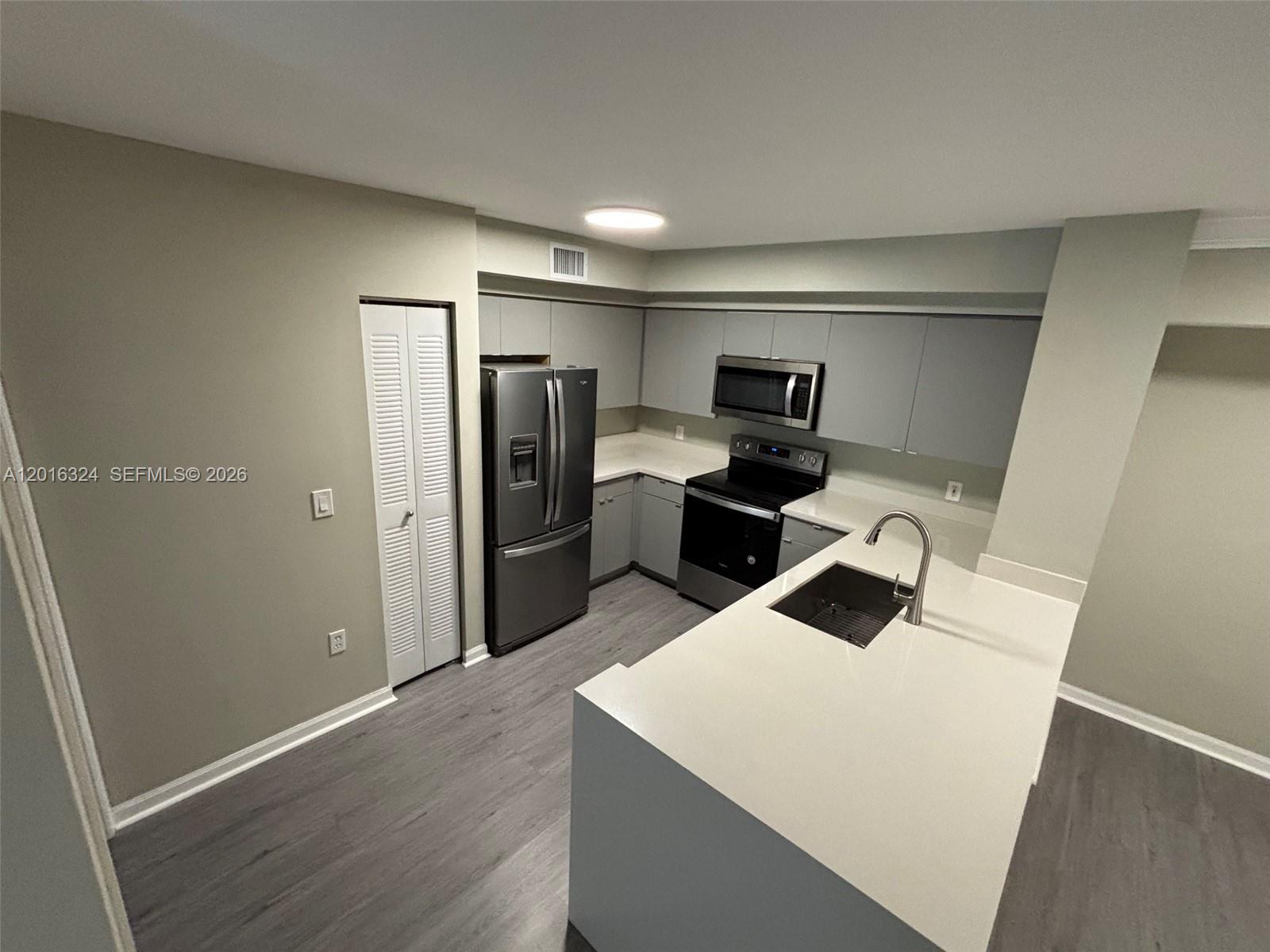 A modern kitchen features gray cabinets, stainless steel appliances, and a white quartz island countertop — 1900 Van Buren St # 201B, Hollywood FL 33020, HOLLYWOOD, FL