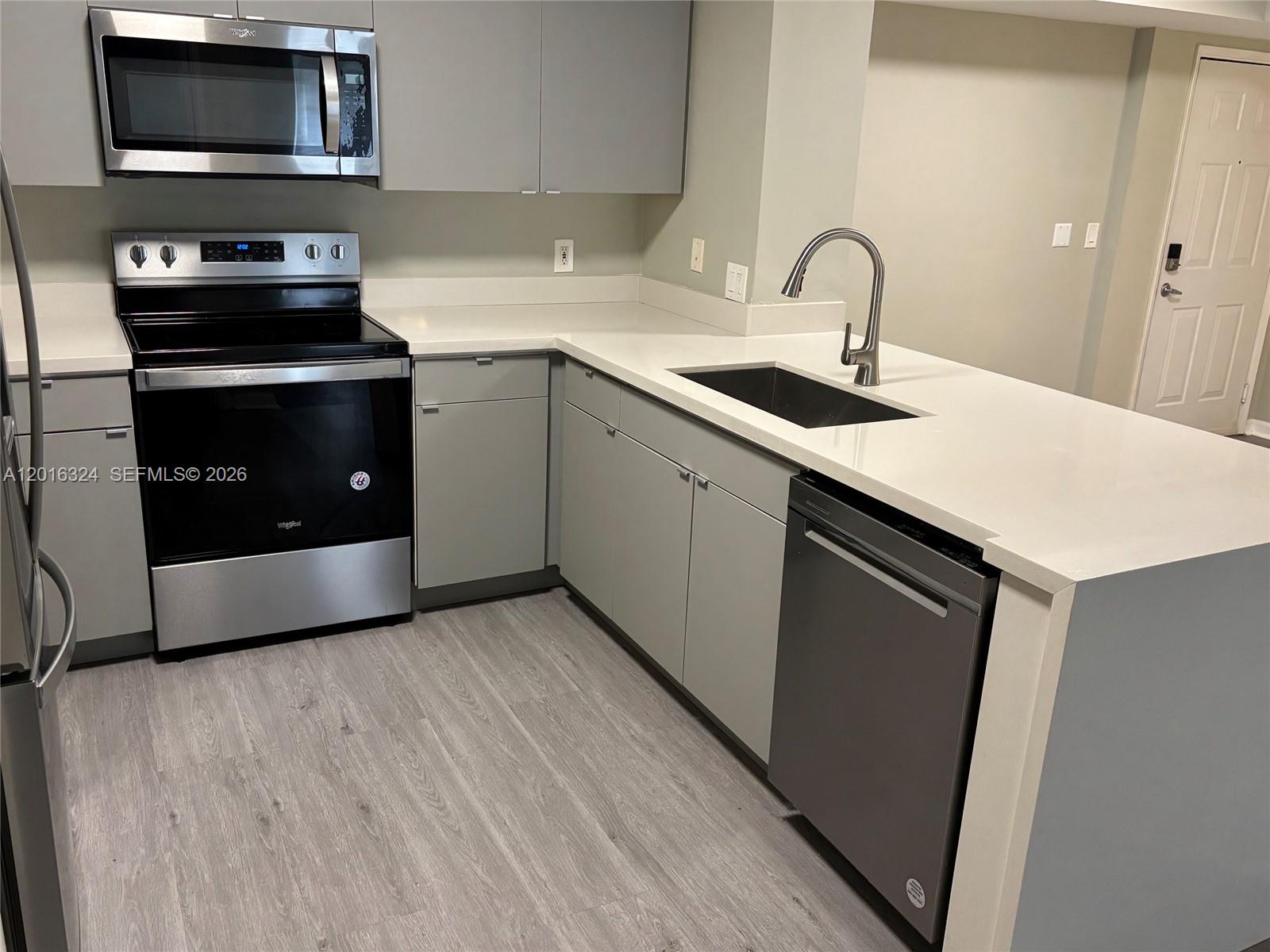 A modern kitchen features gray cabinets, stainless steel appliances, and white countertops — 1900 Van Buren St # 201B, Hollywood FL 33020, HOLLYWOOD, FL