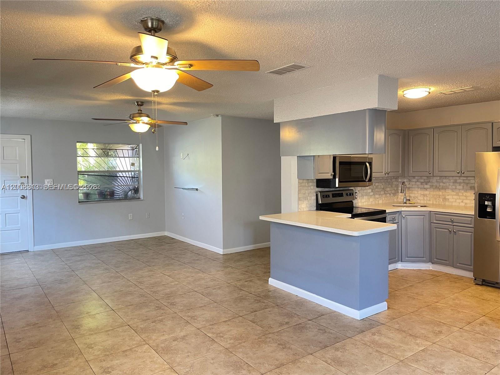 An open-concept living area features a kitchen with gray cabinets, a breakfast bar, and tile flooring — 1074 NW 27th St, Miami FL 33127, MIAMI, FL