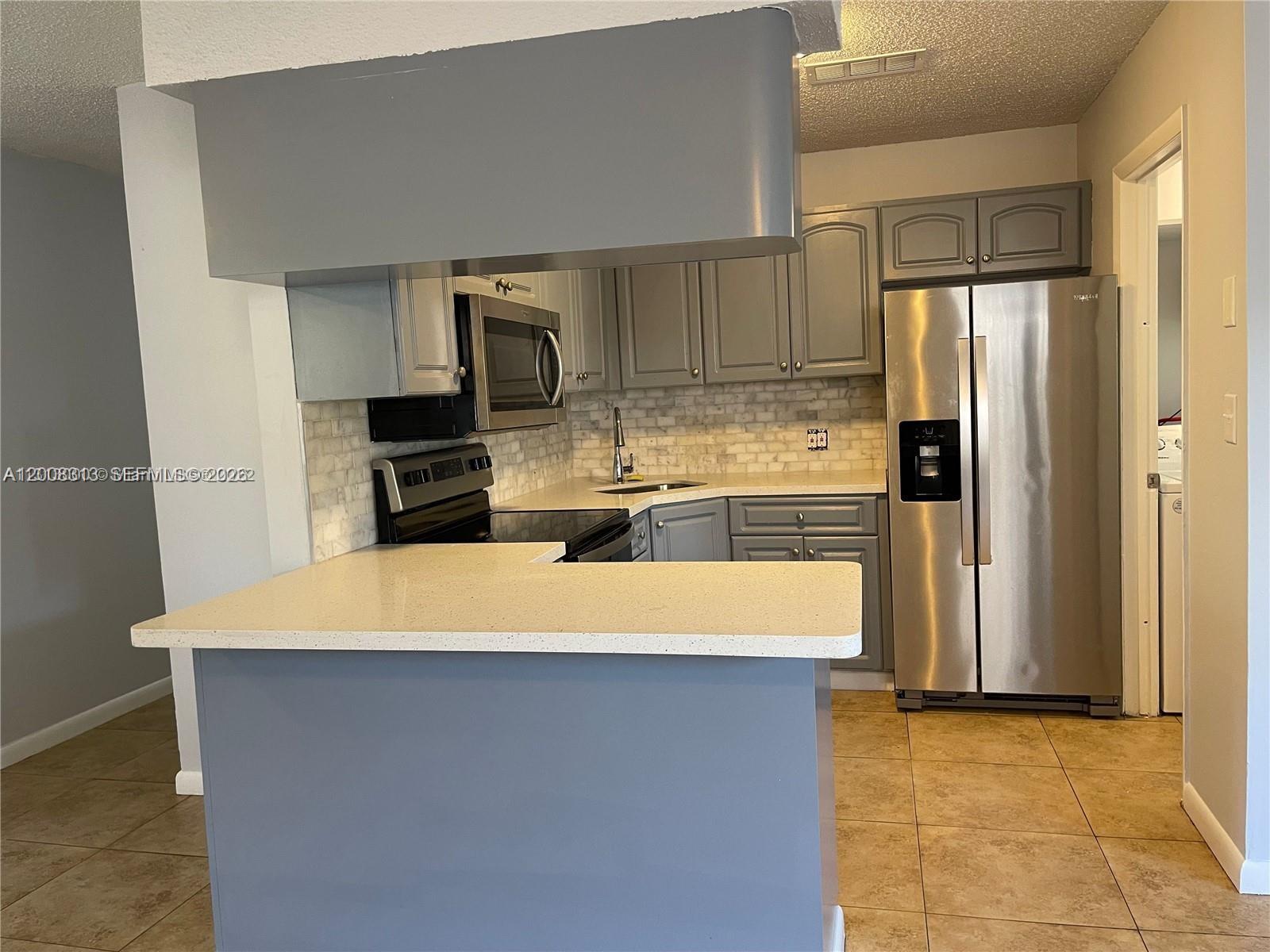 A kitchen features gray cabinets, stainless steel appliances, a light countertop, and a tiled backsplash — 1074 NW 27th St, Miami FL 33127, MIAMI, FL