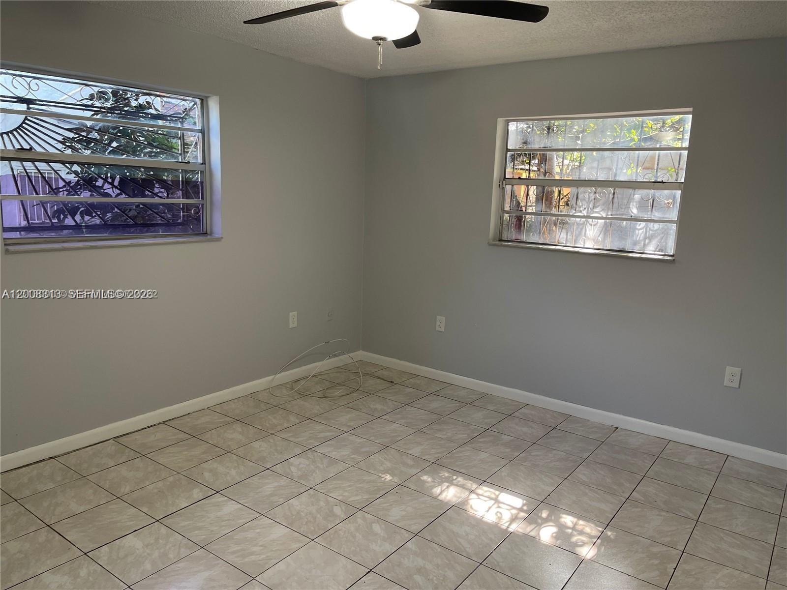 An empty room features light gray walls, tiled flooring, a ceiling fan, and two windows — 1074 NW 27th St, Miami FL 33127, MIAMI, FL