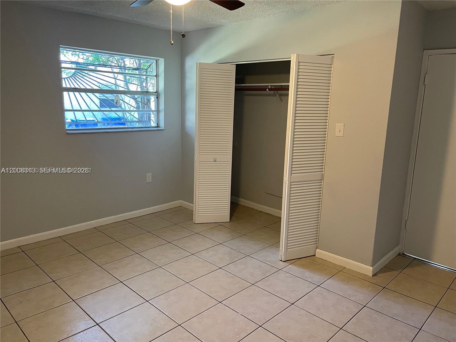 A bedroom features light gray walls, beige tile flooring, a closet with louvered doors, and a window — 1074 NW 27th St, Miami FL 33127, MIAMI, FL