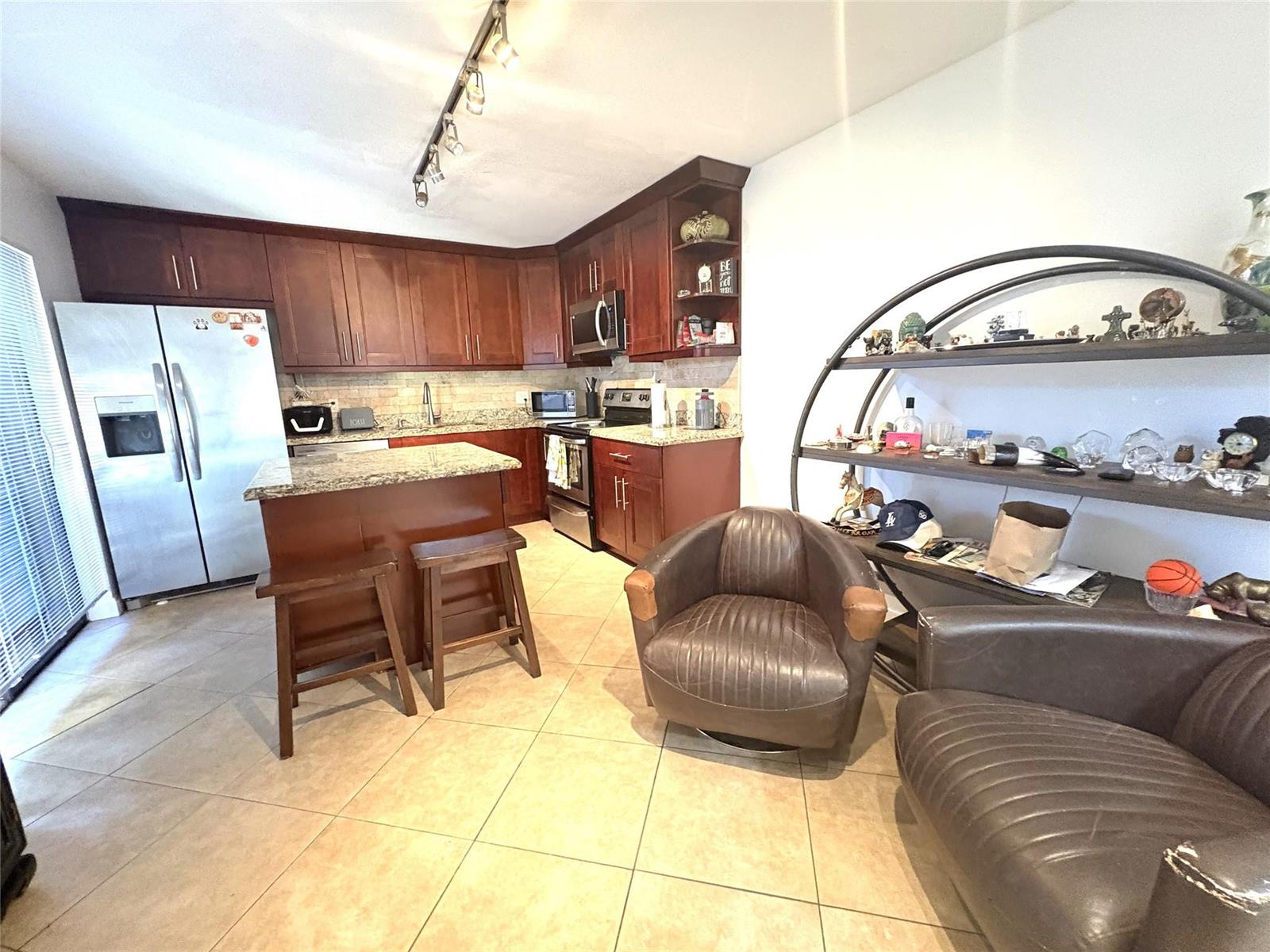 A kitchen with dark wood cabinets, granite countertops, and two leather chairs in the foreground — 294 Arabian Road # 294, Palm Springs FL 33461, PALM SPRINGS, FL