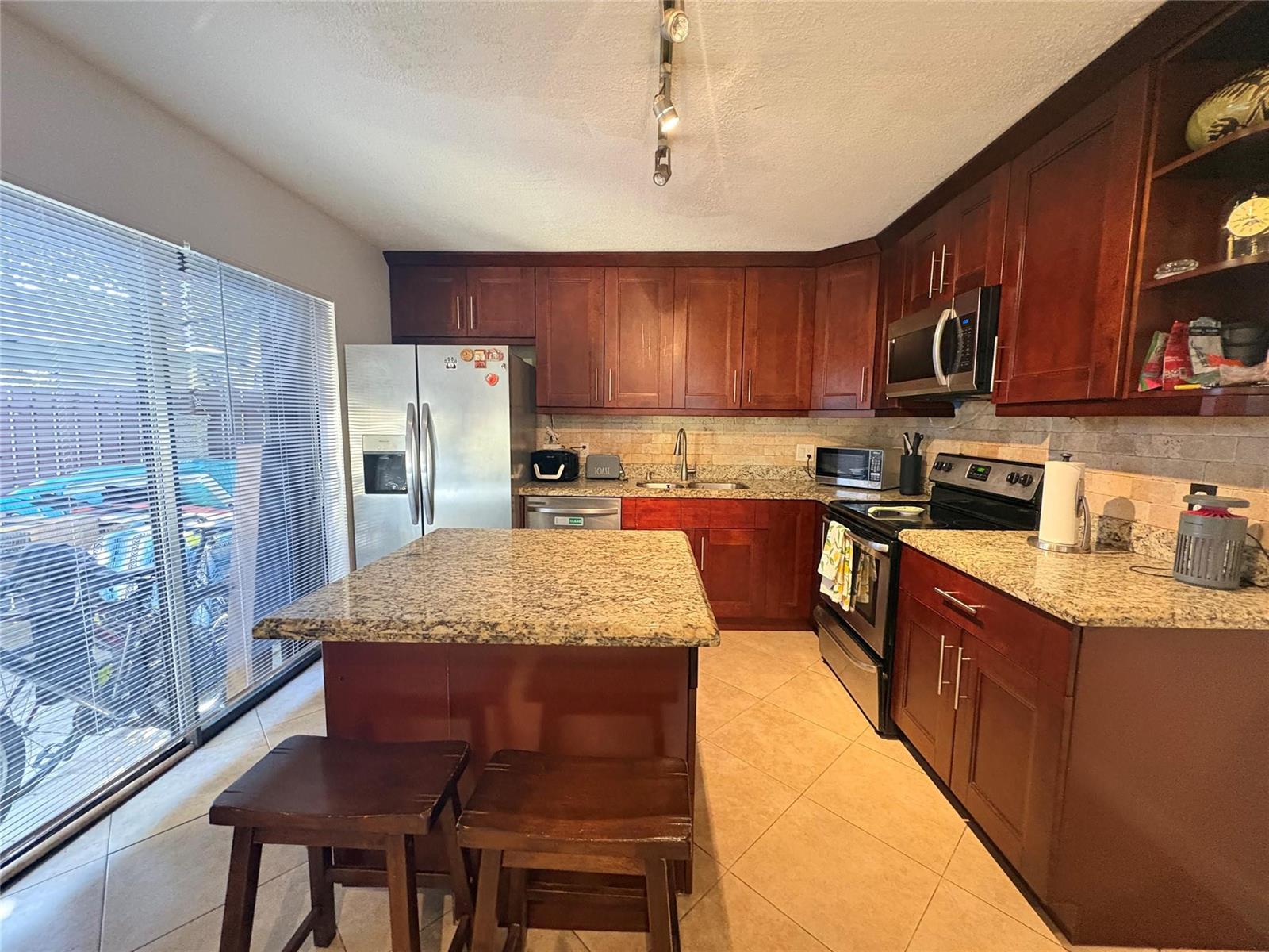 A kitchen features dark wood cabinets, granite countertops, a center island, and stainless steel appliances — 294 Arabian Road # 294, Palm Springs FL 33461, PALM SPRINGS, FL