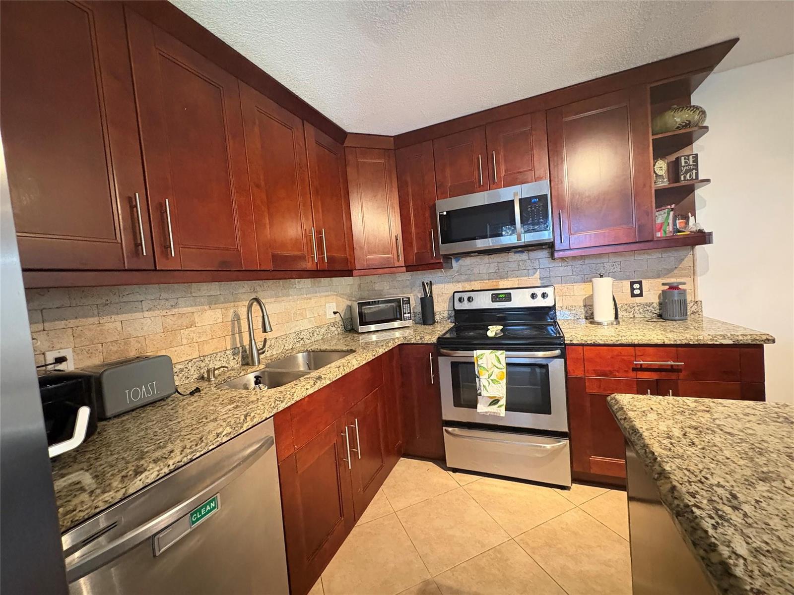 A kitchen features dark wood cabinets, granite countertops, stainless steel appliances, and a tiled backsplash — 294 Arabian Road # 294, Palm Springs FL 33461, PALM SPRINGS, FL