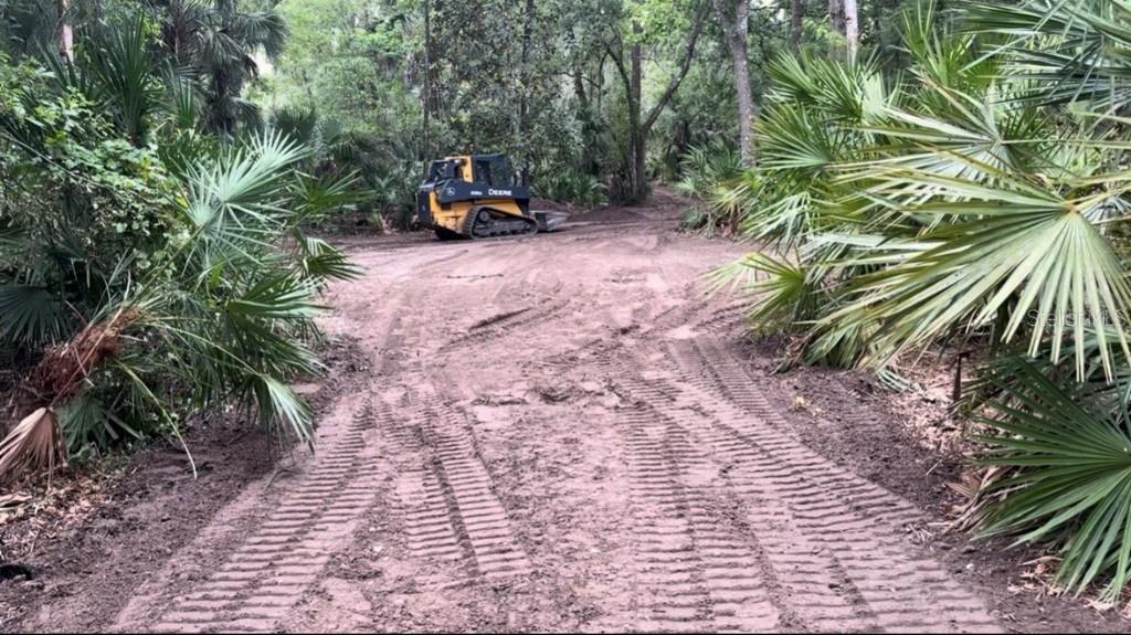 A John Deere bulldozer sits on a cleared dirt path through a wooded area — 901 SHOALS LANDING DRIVE, BRANDON, FL