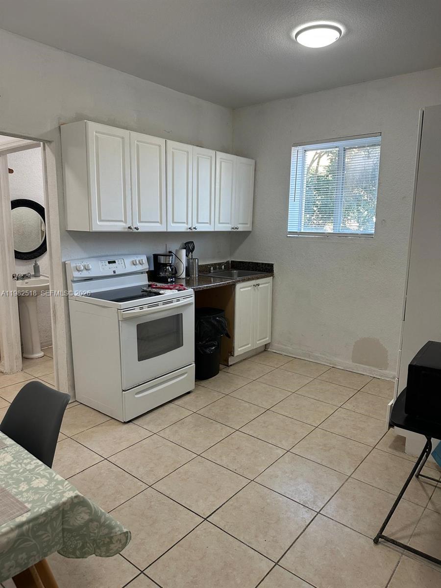 A small kitchen features white cabinets, a white stove, and a window with blinds — 1021 NW 3rd St # 201, Miami FL 33128, MIAMI, FL