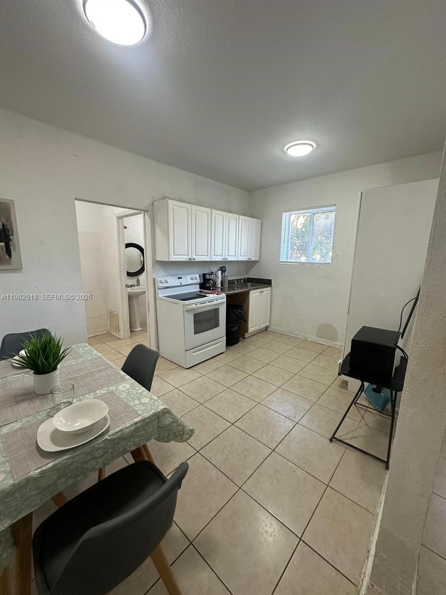This kitchen features white cabinets, a white stove, tiled floors, and an adjacent dining area — 1021 NW 3rd St # 201, Miami FL 33128, MIAMI, FL