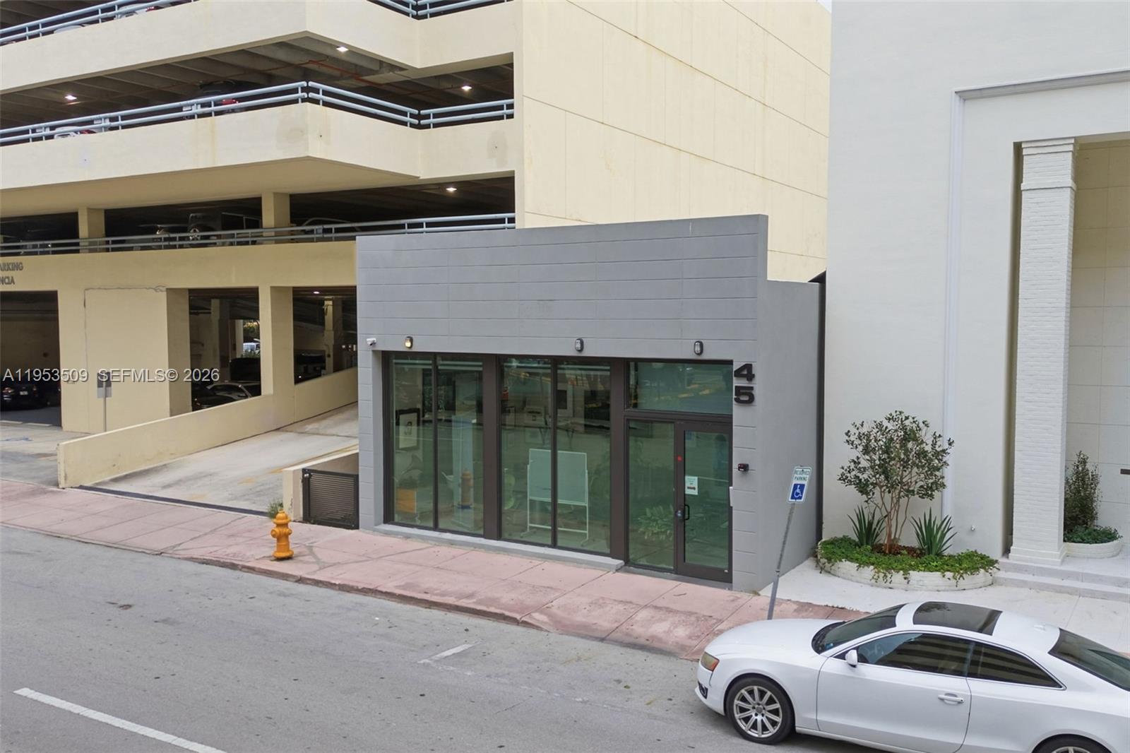A small, gray, single-story commercial building sits between a parking garage and a white structure — 45 Valencia Ave, Coral Gables FL 33134, CORAL GABLES, FL