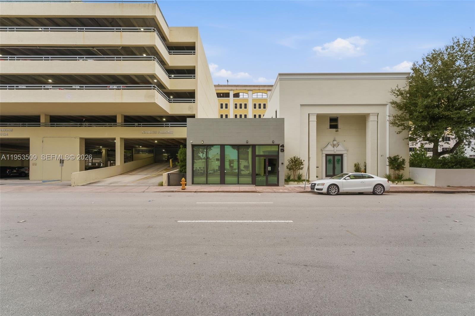 An exterior view shows a modern storefront building next to a parking garage and classical structure — 45 Valencia Ave, Coral Gables FL 33134, CORAL GABLES, FL
