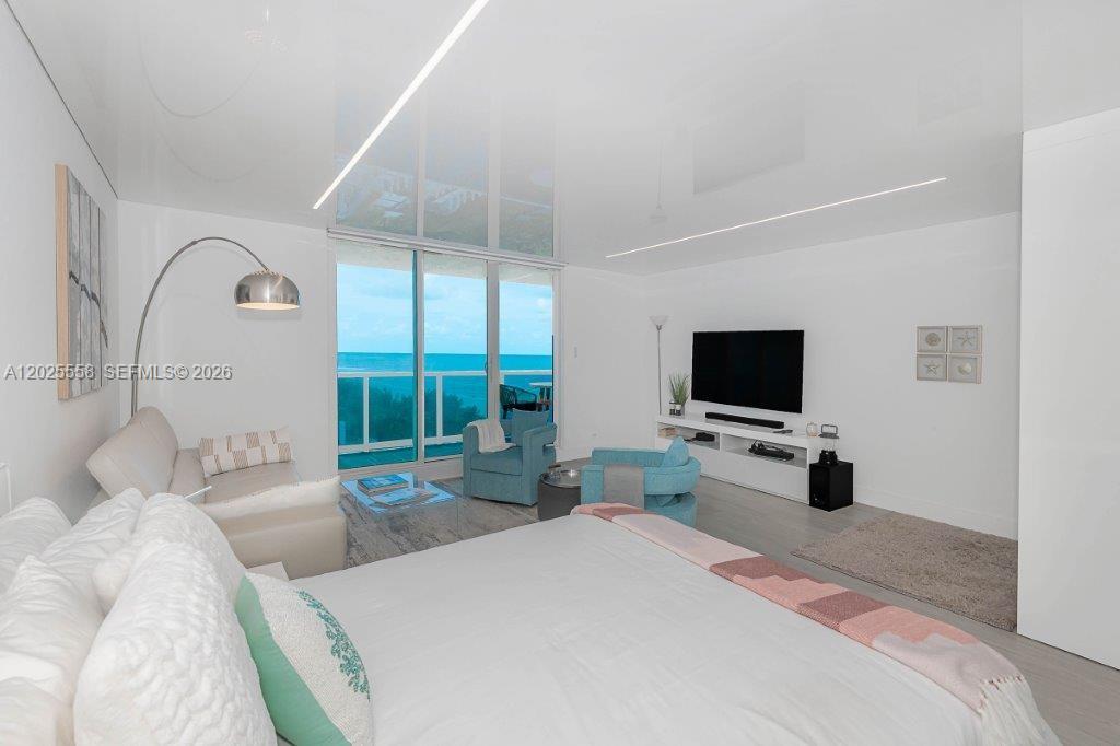 A bright bedroom features a large bed, a seating area, and floor-to-ceiling windows overlooking the ocean — 2301 Collins Ave # 811, Miami Beach FL 33139, MIAMI BEACH, FL