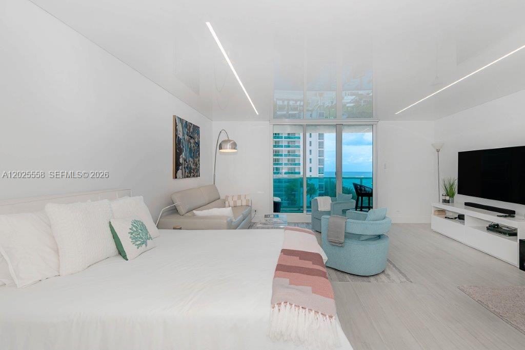 A modern bedroom features white walls, a large bed, seating area, and floor-to-ceiling balcony windows — 2301 Collins Ave # 811, Miami Beach FL 33139, MIAMI BEACH, FL