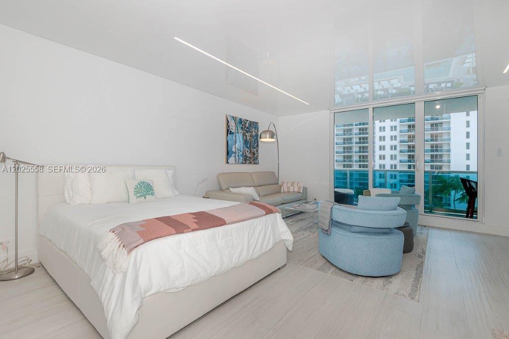 A bedroom features a bed, a sofa, a blue armchair, and floor-to-ceiling windows — 2301 Collins Ave # 811, Miami Beach FL 33139, MIAMI BEACH, FL