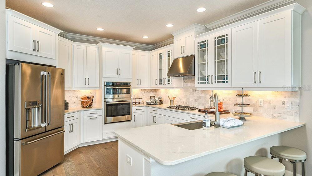 A modern kitchen features white cabinetry, stainless steel appliances, a marble backsplash, and a peninsula — 7008 FOXBORO WAY, NOKOMIS, FL