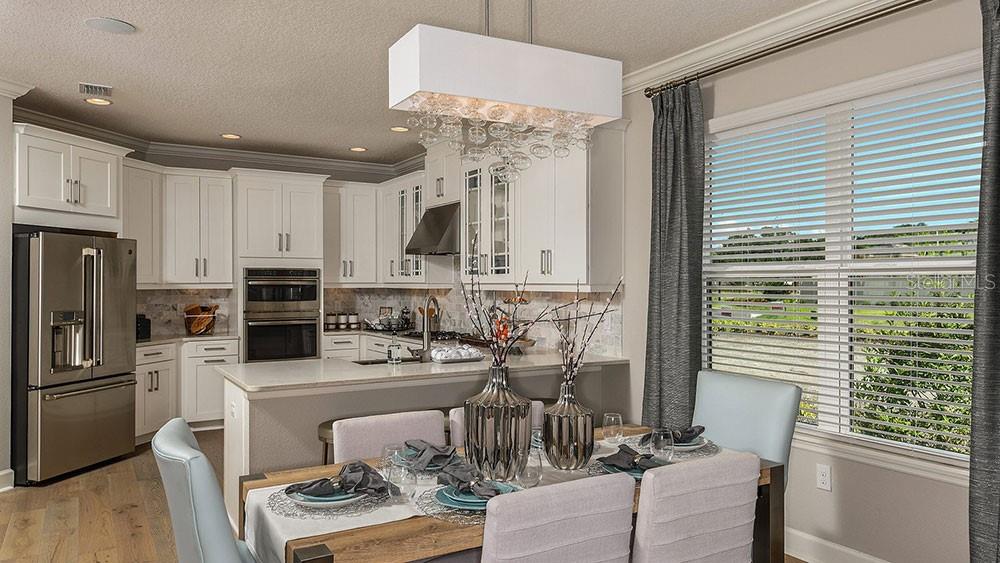 A kitchen with white cabinets and stainless steel appliances overlooks a dining area with seating — 7008 FOXBORO WAY, NOKOMIS, FL