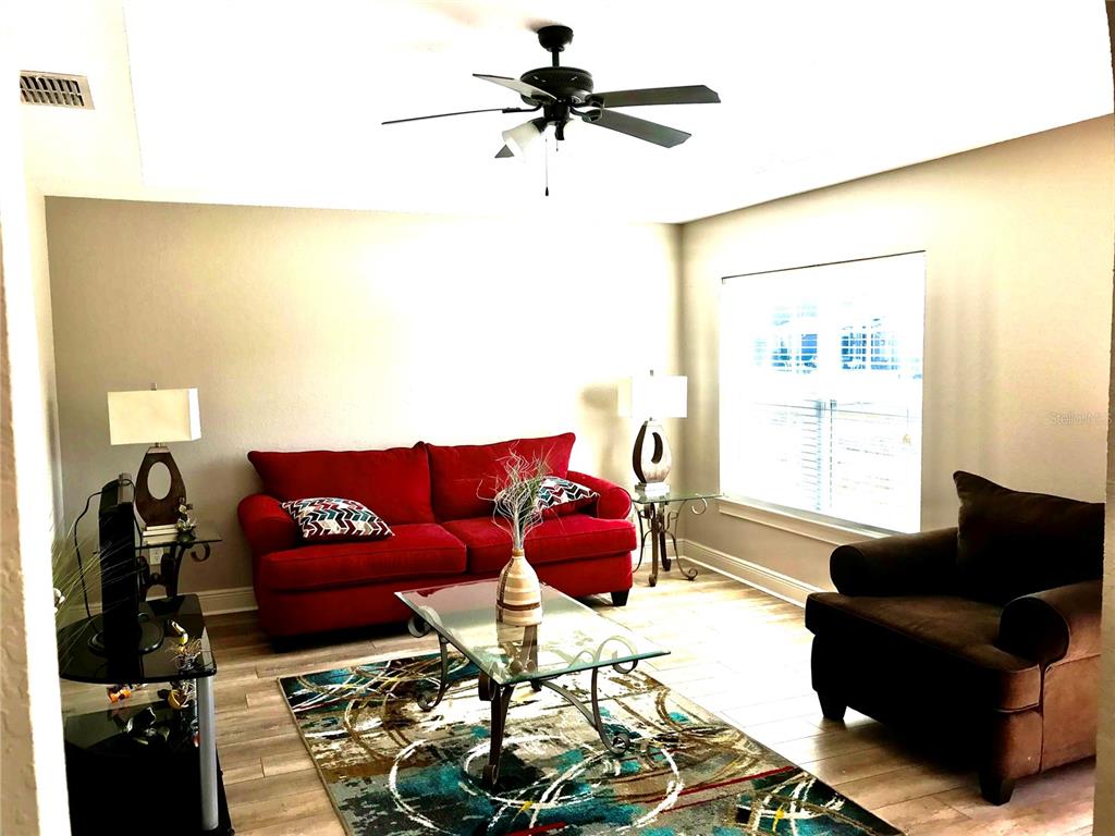 A living room features a red sofa, a brown armchair, a glass coffee table, and wood-look flooring — 4195 SW 114TH STREET, OCALA, FL