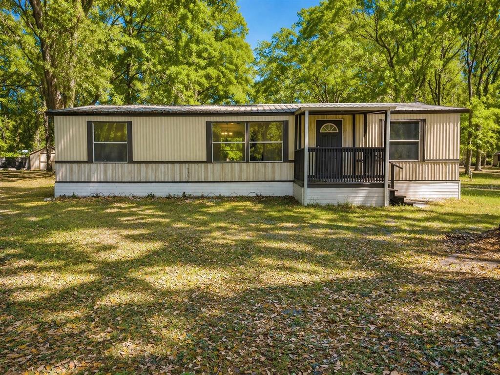 A single-story mobile home with tan metal siding and a small front porch sits outdoors — 2414 NW 121ST AVENUE, GAINESVILLE, FL