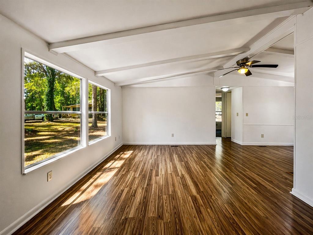 A bright living room features white vaulted ceilings, wood-look flooring, and large windows — 2414 NW 121ST AVENUE, GAINESVILLE, FL