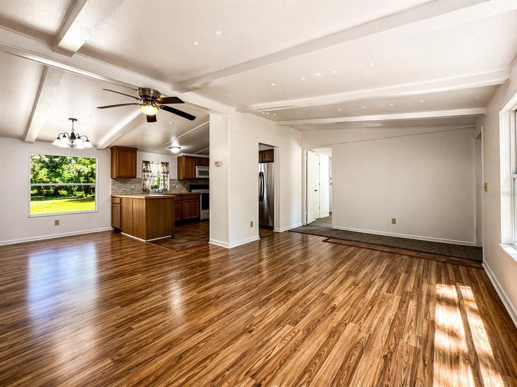 A living room with wood-look flooring and exposed ceiling beams opens to a kitchen area — 2414 NW 121ST AVENUE, GAINESVILLE, FL