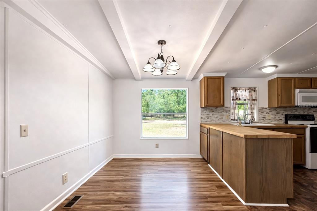 A dining area with wood-look flooring, a chandelier, and an adjacent kitchen with wooden cabinets — 2414 NW 121ST AVENUE, GAINESVILLE, FL