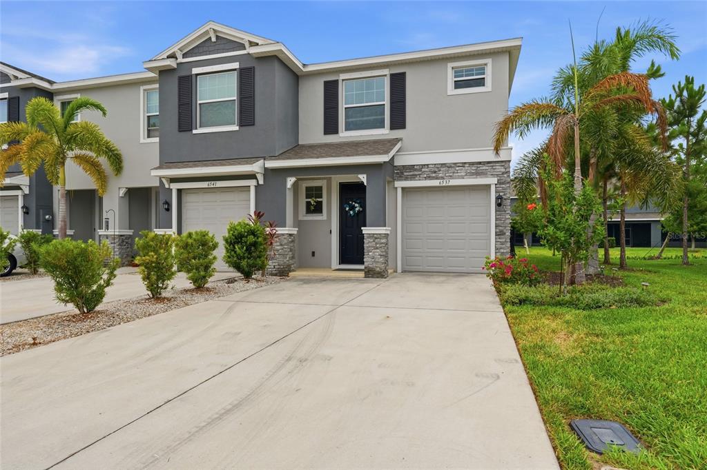 A two-story townhouse with a gray exterior, stone accents, and two attached garages — 6537 SERENITY FALL LANE, SARASOTA, FL