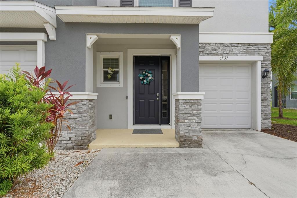 A gray townhouse exterior features a stone-accented facade, a dark front door, and a garage — 6537 SERENITY FALL LANE, SARASOTA, FL