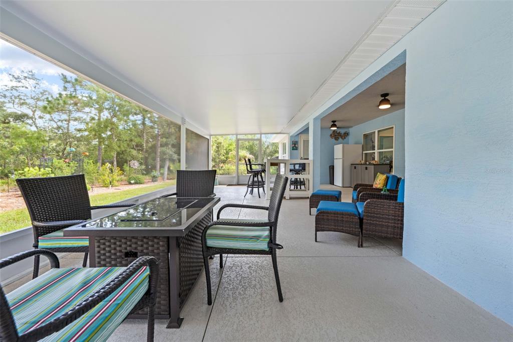 A covered patio features wicker furniture, a fire pit table, and a view of trees — 8 DAHLIA CIRCLE S, HOMOSASSA, FL