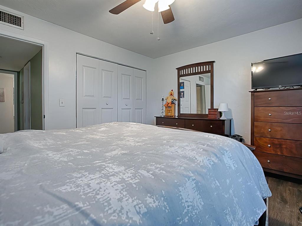 A bedroom features a bed, a dresser with a mirror, and a ceiling fan — 24104 SANDALWOOD DRIVE UNIT 104, WILDWOOD, FL