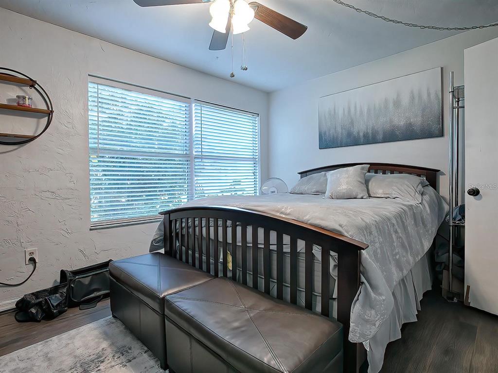 A bedroom features a bed with a dark wood frame, a storage bench, and blinds — 24104 SANDALWOOD DRIVE UNIT 104, WILDWOOD, FL