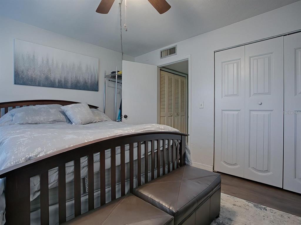 A bedroom features a wooden bed frame, a leather storage bench, and white closet doors — 24104 SANDALWOOD DRIVE UNIT 104, WILDWOOD, FL
