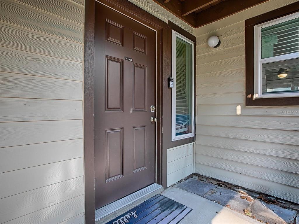 A brown front door with a small window and a welcome mat on a porch — 24104 SANDALWOOD DRIVE UNIT 104, WILDWOOD, FL