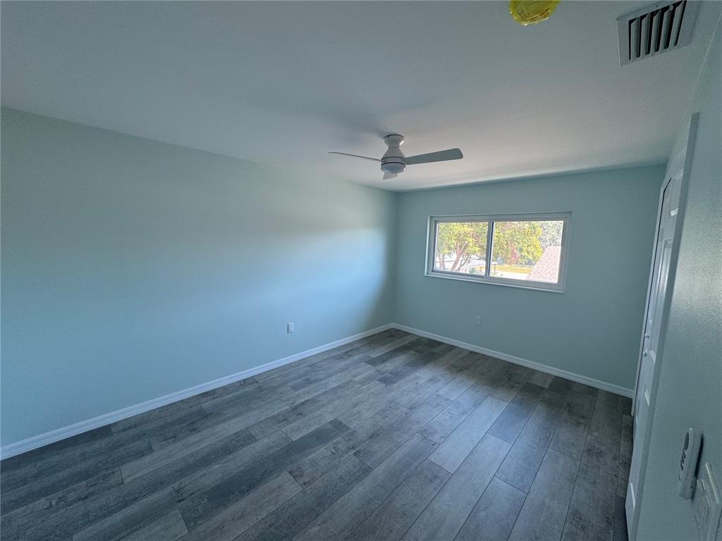 An empty bedroom features light blue walls, gray wood-look flooring, and a ceiling fan — 1258 BARBARA DRIVE UNIT 202, VENICE, FL
