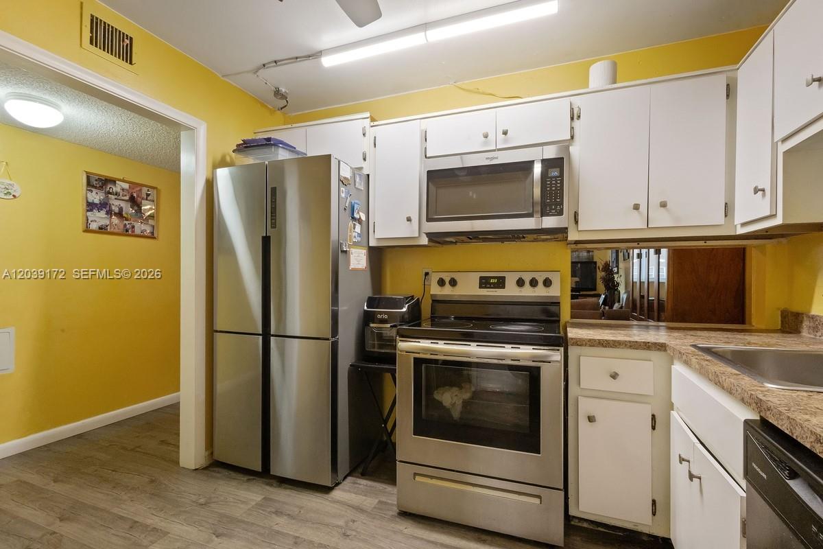 A kitchen features yellow walls, white cabinets, stainless steel appliances, and wood-look flooring — 2271 NW 48th Ter # 112, Lauderhill FL 33313, LAUDERHILL, FL