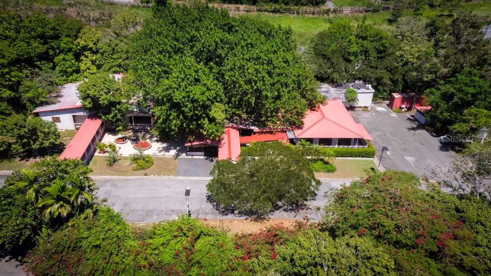 An aerial view shows a building with a red metal roof surrounded by lush trees — 127 KM 4.3 BO. QUEBRADAS AVENUE, GUAYANILLA, PR