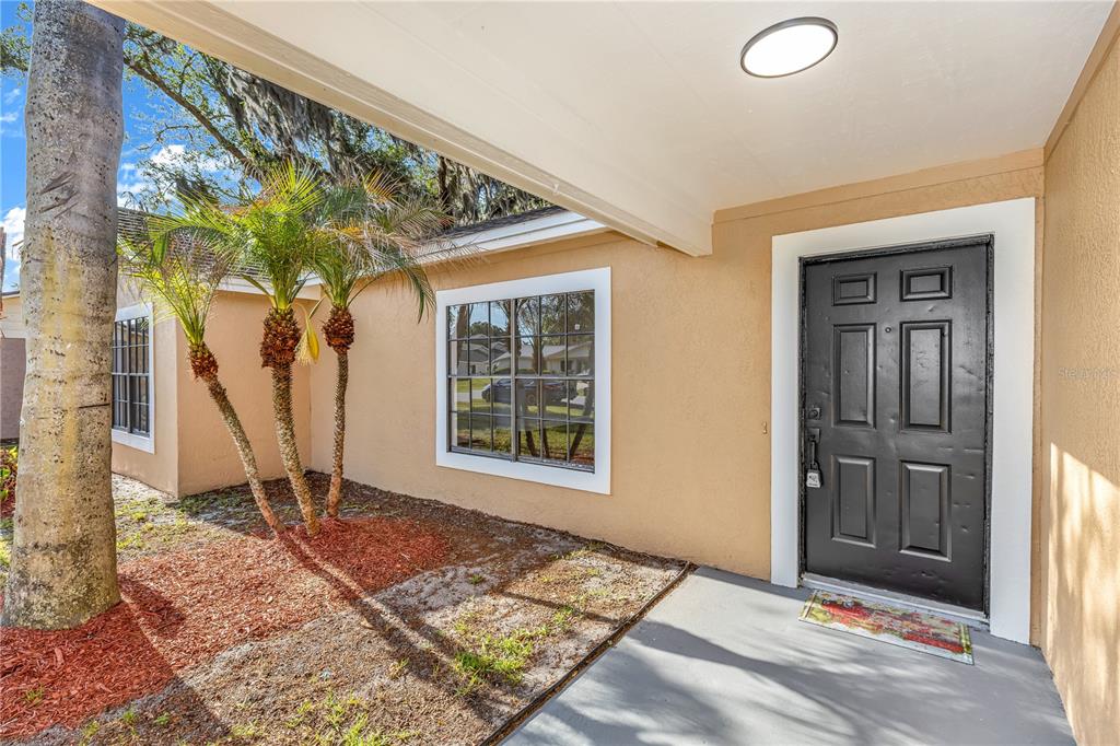 A tan house exterior features a black front door, a window, and small palm trees — 4845 HAWLEY ROAD, COCOA, FL
