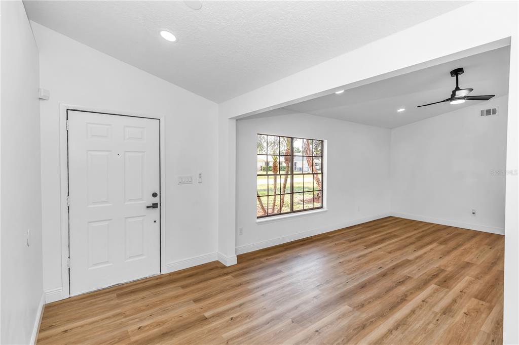 An empty living room features white walls, light wood-look flooring, a ceiling fan, and a window — 4845 HAWLEY ROAD, COCOA, FL