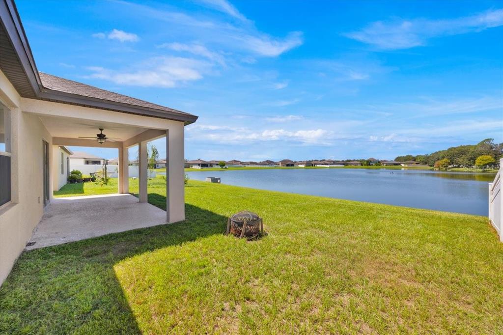 A covered patio overlooks a grassy backyard and a large lake under a blue sky — 8755 RINDGE ROAD, POLK CITY, FL